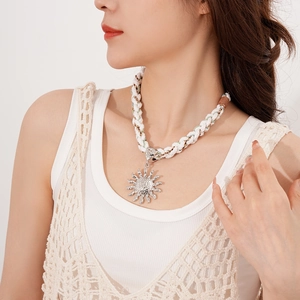 Close-up of white woven rope necklace with a large silver sun pendant on a model