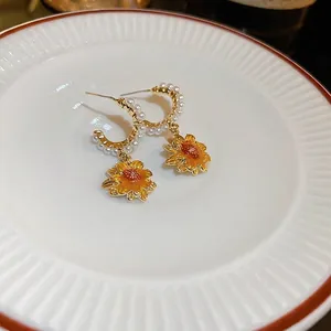 Golden sunflower earrings with white pearls and yellow enamel in a ceramic dish