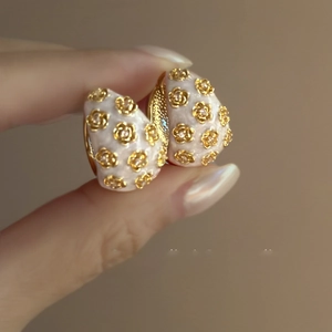 Detailed close-up of C-shaped earrings with white enamel and golden flower motifs