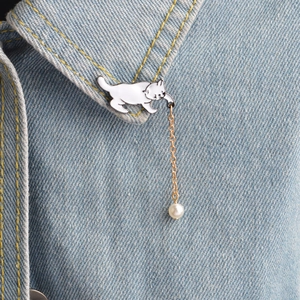 Cartoon white enamel cat brooch with gold chain and pearl on blue denim shirt