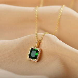 Elegant gold titanium necklace with square emerald pendant on beige silk background