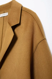 Close-up of camel wool coat showing refined collar stitching and fabric texture