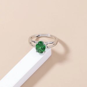 Macro detail of silver ring featuring an oval green gemstone on a white geometric stand