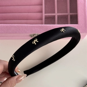 Detail of a black satin headband with gold bow metal accents against pink velvet background