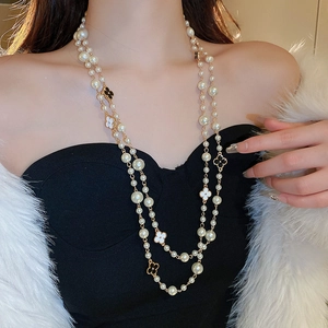 Close-up of double-layer pearl necklace with black and white clover charms on a model