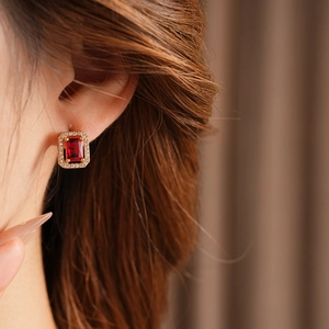 Macro shot of gold square stud earring with red gemstone and diamonds on ear