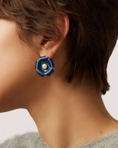 Close-up of blue enamel flower stud earrings with pearl center on a female model's ear
