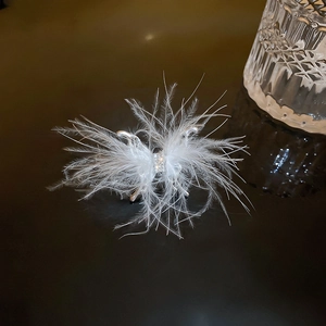 Detailed close-up of white feather hair clip with sparkling rhinestone center and silver base