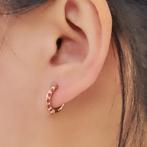 Minimalist gold hoop earrings with pink enamel polka dots shown on a model's ear