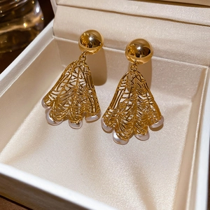 Close-up of golden hollow fan-shaped earrings with pearl accents in a jewelry box