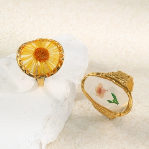 Close-up of golden resin rings with yellow and pink dried flowers on stone base