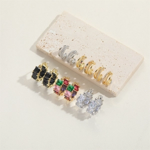 Close-up of assorted gold and silver hoop earrings with zircon stones on stone texture