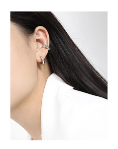 Detail of a minimalist geometric silver ear cuff worn by a model on a white background