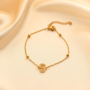 Close-up of golden stainless steel bracelet with a crystal-encrusted letter S pendant