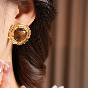 Close-up of vintage golden round tiger eye earrings on female model with retro style