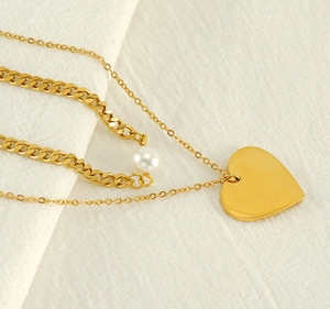 Detail view of double-layer gold necklace featuring heart pendant and white pearl accents