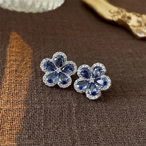 Detail of flower stud earrings featuring blue drop zircons and shimmering silver plating