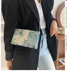 Floral oil painting box bag with silver chain worn by a model in a black blazer