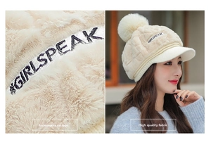 Detail of beige plush knit cap with furry texture, logo embroidery, and large pompom