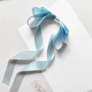 Detailed view of light blue silk satin hair bow with long trailing ribbon and smooth texture