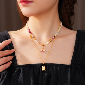 Close-up of vintage enamel bag and gold lock pendants on layered beaded necklaces