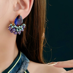 Close-up of teardrop blue zircon stud earrings with matte purple beads on a model