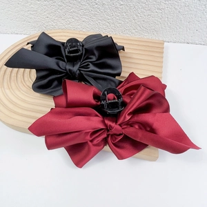 Elegant French satin bow hair claws in black and burgundy on a wooden display stand