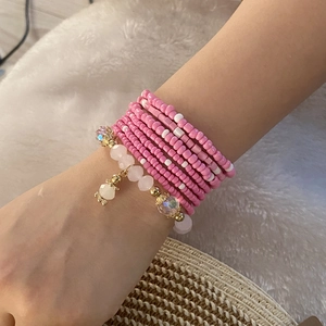 Detail of pink and white multi-layer beaded bracelets with gold charms on wrist