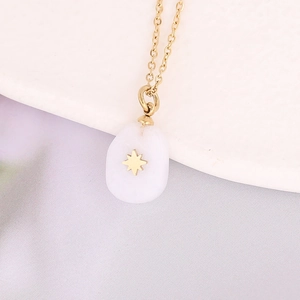 Macro view of gold chain with white stone teardrop pendant featuring a gold star inlay