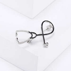 Macro shot of silver metal stethoscope brooch with black enamel details on white background