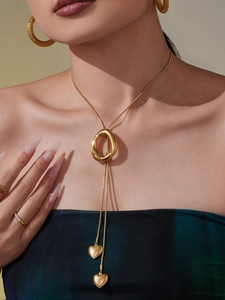 Detail of gold bolo necklace with heart pendants and textured hoop earrings on model