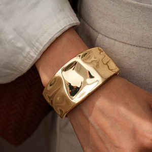 Detail view of a gold-plated wide cuff bracelet with a wrinkled wave geometric texture