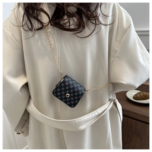 Close-up of black geometric mini bag with gold chain strap on white coat