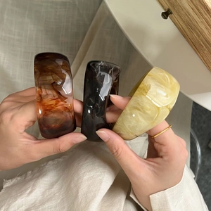 Detailed view of wide resin bangles in amber and cream marble textures held by hand