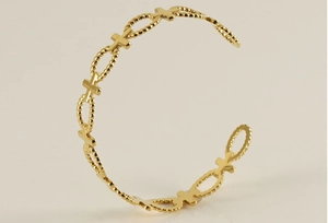 Detailed macro of gold-plated cross bracelet with hollow oval links and rope-textured details