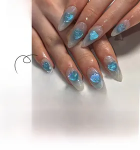 Detail of almond-shaped nails with blue marble pattern and 3D glitter heart accents
