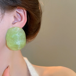 Close-up of a light green translucent resin earring with textured oval design on a model