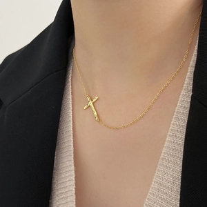 Close-up of golden horizontal cross necklace with hammered texture on a female model