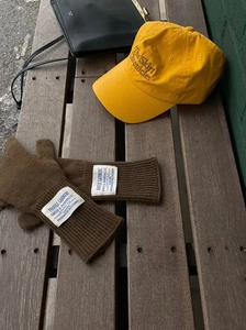 Gorra de béisbol amarilla y guantes de punto marrones sobre un banco de madera rústico