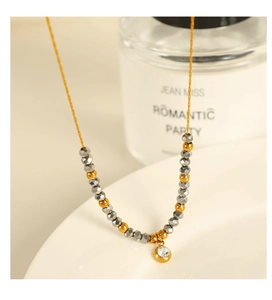 Detail of beaded necklace featuring golden and dark grey beads with a round zircon pendant