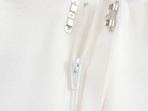 Dettaglio dei pantaloni bianchi con cerniera nascosta e chiusura con gancio metallico