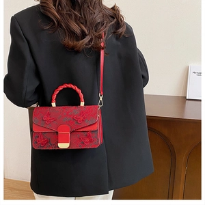 Détail d'un sac à main rouge brodé avec boucle dorée et poignée en corde torsadée
