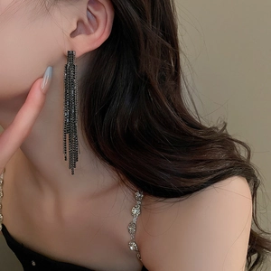 Close-up of elegant black tassel earrings with sparkling rhinestones worn by a model