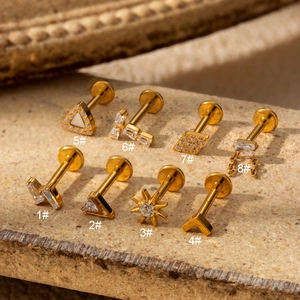 Detail of eight golden G23 titanium labret studs with zircon and opal on stone surface
