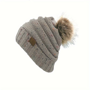 Détail de bonnet tricoté gris clair moucheté avec un gros pompon marron moelleux