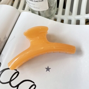 Detail of orange matte claw clip on white book page with natural aesthetic lighting