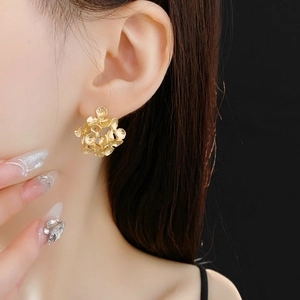 Close-up of a model wearing elegant gold floral cluster earrings with metallic finish
