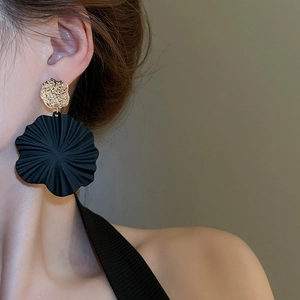 Nahaufnahme von Model mit großen schwarzen Spiralblüten-Ohrringen und goldener Hammerschlag-Optik