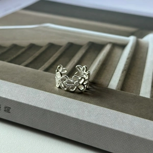 Detailed close-up of a silver hollow flower ring with crystal accents on a grey prop