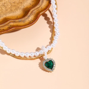 Detail of layered gold snake chain and pearls with a heart-shaped green zircon pendant